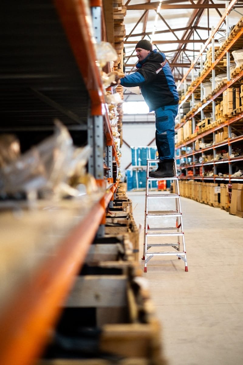 Photo by Kseniia Ilinykh Warehouse worker on a ladder checking stock on high racking, representing supply chain recruitment
