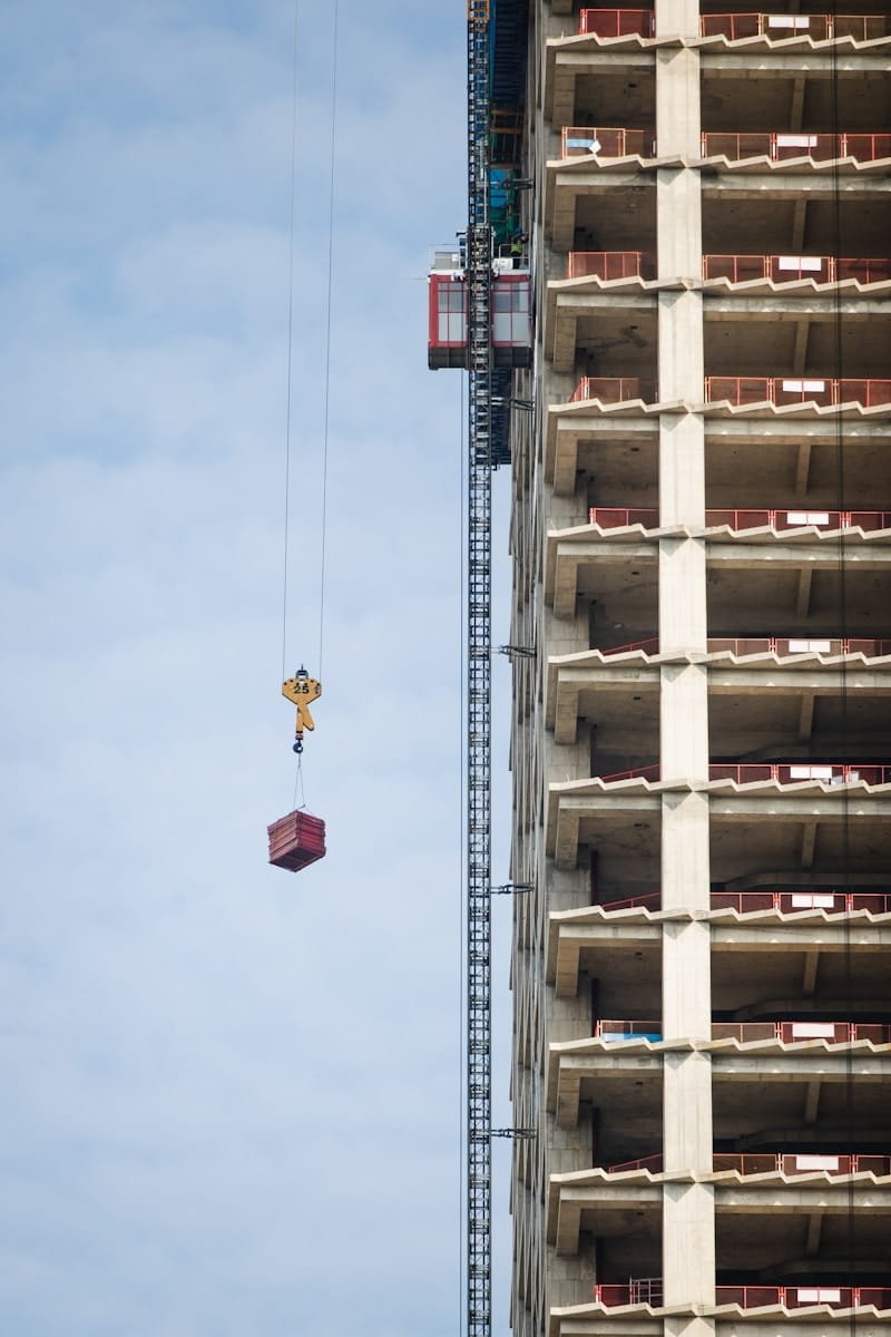 Crane lifting materials beside a high-rise concrete building under construction, representing structural engineer recruitment