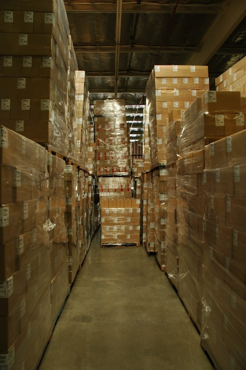 Warehouse aisle stacked with cardboard boxes, representing supply chain and procurement recruitment