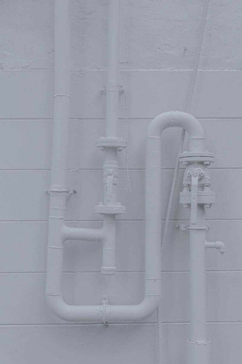 Photo by Yena Kwon White plumbing pipework and valves mounted on a wall, representing the skilled plumbers supplied by our plumber recruitment agency