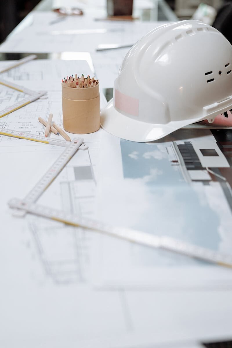 Photo by Thirdman A detailed view of an architect's desk with plans, a hard hat, and drafting tools.